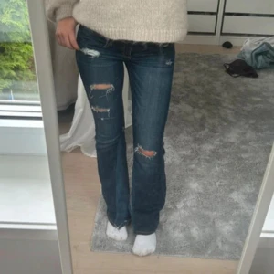 Hollister jeans  - Säljer ett par mörkblå bootcut jeans med slitna detaljer och hål på låren. Jeansen har snygga broderade bakfickor med kontrastsömmar och låg midja. Materialet är klassisk denim och passformen är normal. Perfekta för dig som gillar en avslappnad och trendig look. Waist 24, length 31❤️ måtten är: innerbensmått, 73 cm, midjemått, 33 cm