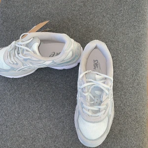 ASICS vita sneakers med mesh och skinn - Snygga vita ASICS sneakers med ljusgrå och silverdetaljer. Skorna har en chunky sula, meshpaneler för extra ventilation och detaljer i syntet och skinn. Klassisk snörning och rund tå. Perfekta för dig som gillar sportig och fräsch stil.