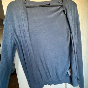 Blå kofta från 157, storlek S - Snygg grå kofta från 157 i storlek S. Den har långärmade och öppen front utan knappar, perfekt att slänga över en t-shirt eller linne. Materialet känns mjukt och lätt, med ribbade muddar vid ärmslut och nederkant. Enkel och stilren design som funkar till många outfits. Klippt själv!