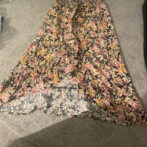 Blommig långkjol från Bik Bok - Supersöt långkjol från Bik Bok med blommigt mönster i rosa, gul, beige och svart. Kjolen har en flowy passform och resår i midjan för extra komfort. Perfekt för dig som gillar färg och vill sticka ut lite extra.