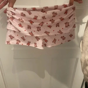 Söta rosa shorts med nallemönster - Supergulliga ljusrosa shorts med brunt nallemönster och små röda hjärtan. De har en lös passform och rynkade detaljer i sidorna. Perfekta för sommaren eller mysiga dagar hemma.