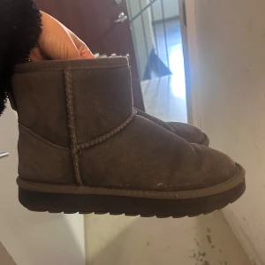 Gråa uggs - Mysiga bruna boots i mocka med platt sula och rund tå. Skorna har en klassisk enkel design och är fodrade på insidan för extra värme. Perfekta för kalla dagar och passar till många olika outfits.