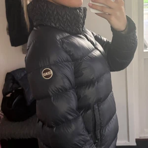 Svart Colmar pufferjacka med huva - Snygg svart pufferjacka från Colmar med quiltade detaljer på krage och ärmslut. Jackan har hög krage, avtagbar huva och två fickor med dragkedja. Klassisk logga på ärmen och ryggen och stilren design. Passar S. Jättefint skick, knappt använd. Hör av dig vid frågor💕