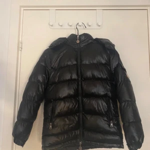 Svart Moncler pufferjacka med huva - Intresskoll på min svart pufferjacka från Moncler med glansig finish och huva. Jackan har dragkedja framtill, två fickor med dragkedja och Moncler-logga på ärmen. Perfekt för kalla dagar och riktigt snygg streetstil. Kan tänka mig o byta mot en Moncler maya i xs/ xxs 