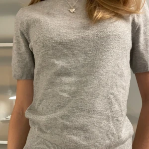 Grå stickad tröja med kort ärm - Supermjuk grå stickad tröja med korta ärmar och rund hals. Tröjan har ribbade muddar vid ärmslut och nederkant, vilket ger en snygg och enkel look. Perfekt att styla med jeans eller kjol för en chill vibe. Hör av er om ni har frågor! Säljer då den inte får användning. 🌸
