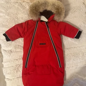 Röd Åkpåse Canada Goose - Säljer en röd åkpåse Canada Goose med fluffig päls runt huvan och två långa dragkedjor framtill. Jackan har svart foder, praktisk ficka på magen och logotyp på ärmen. Helt ny oanvänd!! Nypris 590 euro , ~6900kr, säljes nu för endast 2000kr! Kvitto finns. Exklusiv o unik åkpåse som inte finns att få tag på mer! Vilket betyder att andrahandsvärdet kommer stiga! Storlek 0-3 månader men passar 0-6 månader 