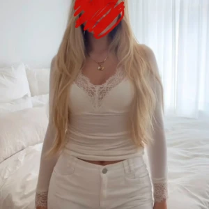 Vit långärmad tröja från Intimissmi - Säljer en vit långärmad topp med v-ringning och fina spetsdetaljer vid halsringning och ärmslut. Modellen är slim och har en mjuk, stretchig känsla som sitter snyggt på kroppen. Perfekt för dig som gillar en clean och feminin look.