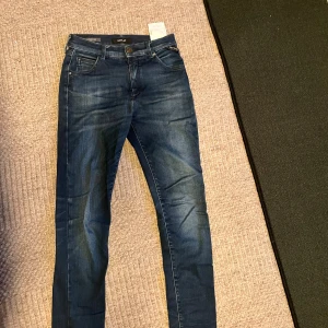 Replay Hyperflex slim jeans blå - Snygga blå Replay Hyperflex jeans med skinny fit och klassisk femficksdesign. Jeansen har en mörk tvätt med lätt slitning och är tillverkade i stretchigt jeansmaterial för extra komfort. Perfekta för dig som gillar en tajt och modern look.