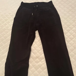 Svarta velourbyxor Juicy Couture XS - Mysiga svarta mjukisbyxor från Juicy Couture i velour med snörning i midjan och fickor både fram och bak med snygga knappar. Köparen står för frakten!