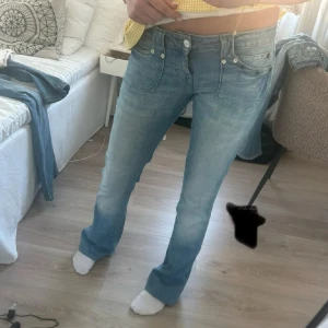 Wrangler bootcut jeans ljusblå - Säljer ett par ljusblå bootcut jeans från Wrangler med klassisk femficksdesign och låg midja. Jeansen har en snygg tvätt och subtila slitningar, samt tydlig Wrangler-logga på bakfickan. Perfekta för dig som gillar retrovibbar och en avslappnad look.