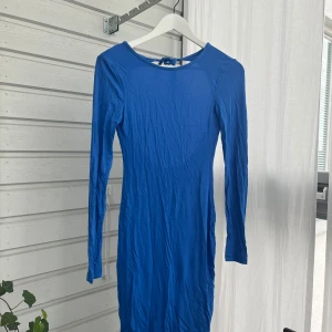 Blå långärmad klänning NLY Trend XS - Snygg blå långärmad klänning från NLY Trend i storlek XS. Modellen är figurnära med rund hals och en djup öppen rygg som knyts med band i nacken. Mjuk och stretchig bomullskvalitet som sitter skönt på kroppen. Perfekt för dig som gillar att sticka ut med en cool ryggdetalj.
