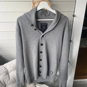 Grå kofta med knappar från Jack & Jones - Snygg grå kofta i märket Jack & Jones premium, som inte längre går att köpa i butik. Jag har endast använt den ett fåtal gånger därav är den i utmärkt skick.  Vid minsta lilla fråga så är det bara att skicka ett meddelande. Mvh/ Leo 
