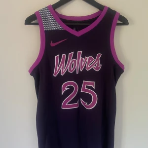 Minnesota Timberwolves D-Rose NBA-tröja - Säljer en officiell Minnesota Timberwolves baskettröja från Nike, med Derrick Rose och nummer 25 på ryggen. Tröjan är mörklila med rosa detaljer och har ett coolt geometriskt mönster på axeln. Perfekt för dig som älskar basket och vill sticka ut med snygg NBA-stil. Självklart äkta.