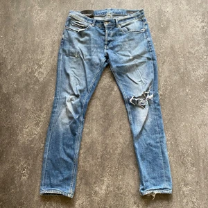 Dondup jeans med slitningar - Säljer ett par blå jeans från Dondup med snygga slitningar och hål på ena knät. Passformen är george och storleken är 33 men skulle säga att den sitter som 32 eller 31. Dessvärre är det hål i grenen (bild 5) och därmed kan priset disskuteras. 