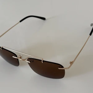 Eytys Avery solglasögon guld/brun - Ett par helt nya Eytys Avery solglasögon med rektangulära brunt glas och tunna guldfärgade metallbågar. Glasögonen har minimalistisk design och ger en modern look! 