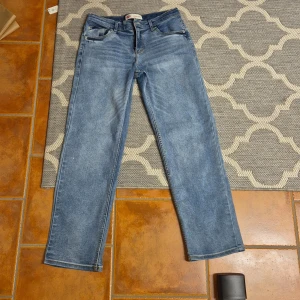 Levi's 501 ljusblå raka jeans - Klassiska Levi's 501 jeans i ljusblå tvätt med raka ben och normal passform. Jeansen har fem fickor, knappgylf och ikonisk läderpatch bak i midjan. Perfekta för en avslappnad och tidlös look.