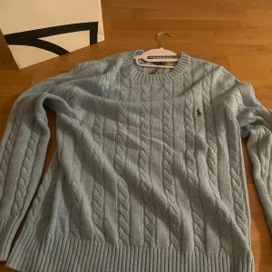 Ljusblå kabelstickad tröja Polo Ralph Lauren (nypris 2400) - Kabelstickad ljusblå tröja från Polo Ralph Lauren med rund halsringning och broderad logga på bröstet. Pris kan diskuteras i dm