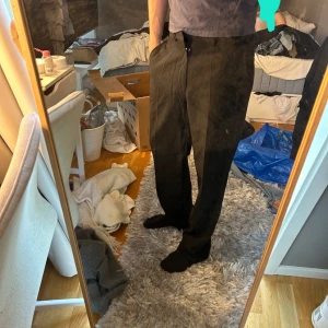 Svarta kostymbyxor  - Säljer ett par svarta kostymbyxor herr. Byxorna är raka i modellen med klassisk passform och tillverkade i 100% ull. Perfekta för dig som gillar stilrena och tidlösa plagg. Snygga pressveck framtill och diskret dragkedja. Trasig ytterknapp framtill den inre funkar.