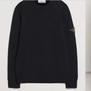 Svart stickad tröja från Stone Island - Svart stickad tröja från Stone Island med klassisk rund hals och ribbade muddar. Tröjan har den ikoniska loggan på vänster ärm som går att ta av med knappar. Perfekt för dig som gillar stilren och clean streetwear.Ny pris 3999kr