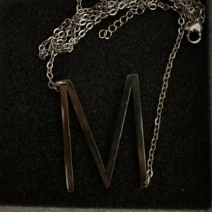 Silverfärgat halsband med bokstaven M - Stilrent halsband i silverfärg med en stor bokstav M som hänge. Kedjan är tunn och smidig, perfekt för att ge en personlig touch till din outfit. Passar dig som vill bära din initial eller ge bort som present.