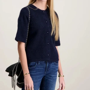 Marinblå stickad kofta - Mysig mörkblå stickad kofta med kort ärm och rund hals. Koftan har knappar framtill och en enkel och stilren design. Aldrig andvänd! Säljer för att den inte kommer till andvändning☺️Pris kan diskuteras