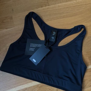 Sporttopp - Sporttopp med sportig racerback-design. Tillverkad i mjukt och stretchigt syntetmaterial som passar perfekt för träning. Enkel och stilren look med breda axelband och diskret logga på etiketten.