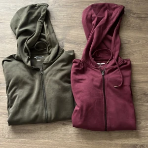 Två hoodies från Jack & Jones,  - Två snygga hoodies från Jack & Jones Essentials i storlek S. En i mörkgrön och en i vinröd färg, båda med dragkedja framtill, huva med snörning och mjukt bomullsmaterial. Perfekta för chill dagar eller när du vill ha en enkel och stilren look. 350 för båda