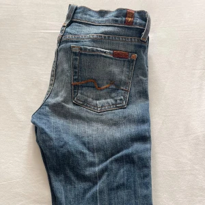 Blå bootcut jeans från 7 For All Mankind - Snygga blå jeans från 7 For All Mankind i klassisk bootcut-modell. Jeansen har fem fickor, orangea kontrastsömmar och ikonisk broderad bakficka. Tillverkade i 98% bomull och 2% polyuretan för en skön stretchig känsla.