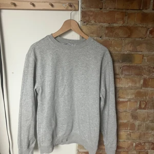 Grå sweatshirt från Weekday - En stilren grå sweatshirt från Weekday med rund halsringning och ribbade muddar. Tröjan har en klassisk passform och är tillverkad i mjuk bomullsmix, perfekt för en avslappnad look. Passar lika bra till jeans som till mjukisbyxor.