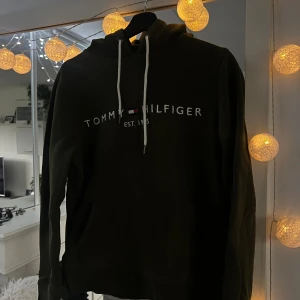 Mörkgrön hoodie från Tommy Hilfiger - Snygg mörkgrön hoodie från Tommy Hilfiger med vit snörning och klassisk logga framtill. Tröjan är i mjuk bomull och har huva samt känguruficka. Hoodien är använd några gånger. 