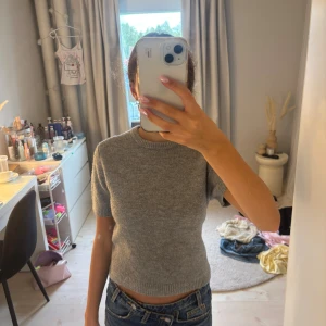 Grå stickad kortärmad tröja från Zara - Supermjuk grå stickad tröja med korta ärmar och rund hals. Perfekt till jeans eller kjol för en chill och stilren look. Ribbstickade detaljer vid hals, ärmslut och nederkant ger en snygg finish.