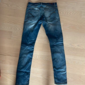 Blå skinny jeans med slitningar dondup  - Snygga blå jeans med skinny fit och slitna detaljer. Jeansen har klassiska bakfickor med dragkedjor och en tvättad look som ger en cool vibe. Perfekta för dig som gillar en smal siluett och streetstyle.
