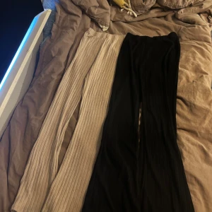 Ribbade vida byxor i svart och beige - Två par ribbade byxor, ett par svarta och ett par beige. Båda har en vid passform och elastisk midja, perfekta för en chill och trendig look. Materialet känns mjukt och stretchigt, vilket gör dem riktigt sköna att ha på sig.   (50kr) för båda 