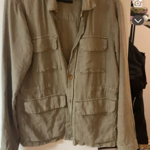 Beige overshirt från Indicode - Stilren beige overshirt från Indicode med fyra stora fickor framtill och knäppning med träfärgade knappar. Jackan har klassisk krage och är långärmad, perfekt för lager-på-lager och chill stil.