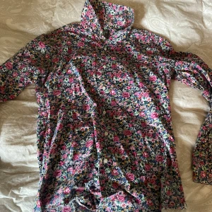 Blommig skjorta från Grand Frank - Färgstark skjorta från Grand Frank med blommigt mönster i rosa, vitt, grönt och blått. Skjortan har klassisk krage, knäppning framtill och långa ärmar. Perfekt för dig som vill sticka ut med en unik och färgglad stil.