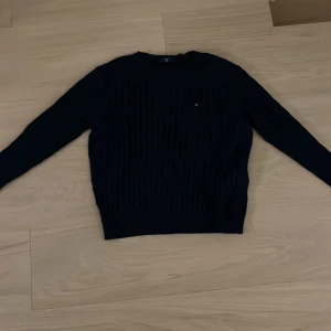 Mörkblå kabelstickad tröja från Gant - Snygg mörkblå kabelstickad tröja från Gant med broderad logga på bröstet. Tröjan har rund halsringning och långa ärmar, perfekt för kyligare dagar. Klassisk och stilren modell som passar till det mesta.