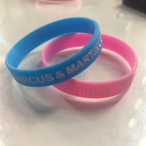 Marcus & Martinus silikonarmband blå/rosa - Två snygga silikonarmband i blått och rosa med texten 'MARCUS & MARTINUS' i vitt. Perfekta för fans som vill visa sitt stöd för sina idoler. Armbanden är mjuka och flexibla, lätta att bära hela dagen. !!pris kan diskuteras!!
