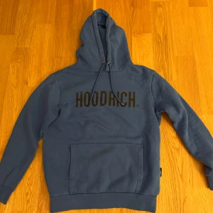 Blå hoodie från Hoodrich med tryck - Blå hoodie från Hoodrich i storlek small med svart tryck över bröstet. Tröjan har huva med snörning och en stor magficka framtill. Mjuk insida och klassisk passform. 