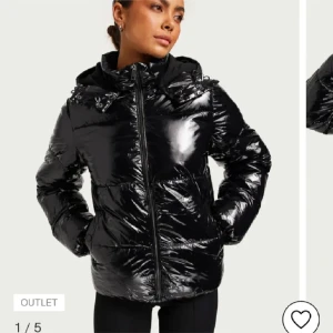Svart glansig pufferjacka från Nelly - Säljer en svart, glansig pufferjacka från Nelly med huva och dragkedja framtill. Jackan är quiltad och har en oversized look, perfekt för kalla dagar. Materialet är syntet och jackan har långa ärmar. Snygg och trendig stil för vintern!