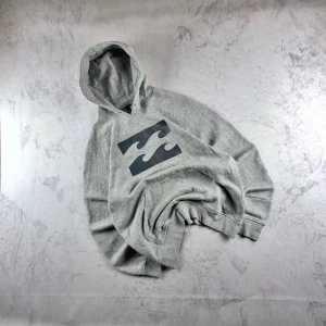 Grå hoodie från Billabong med tryck - Säljer en grå hoodie från Billabong med stort svart våg-tryck på bröstet. Tröjan har huva, ribbade muddar och är tillverkad i mjuk bomullsblandning. Perfekt för chill dagar eller när du vill ha en avslappnad streetstil.
