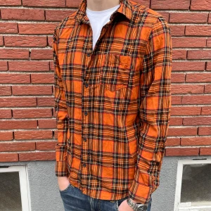 Rutig skjorta  - Säljer en orange rutig skjorta med svarta och gula detaljer. Skjortan har klassisk krage, bröstficka och knäppning framtill. Långärmad modell i mjukt bomullstyg, perfekt för dig som vill sticka ut med färg och mönster. 9/10 skick 🤩 Hör av dig om du har några frågor.