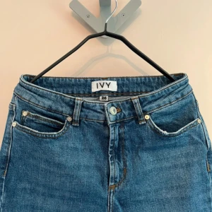 IVY Jeans Johanna - Snygga blå jeans från IVY med klassisk femficksdesign och bootcut-ben. Jeansen har hög midja och är tillverkade i ett mjukt denimtyg med broderad logga på bakfickan. Perfekta för en trendig och avslappnad look. Storlek: 26/28