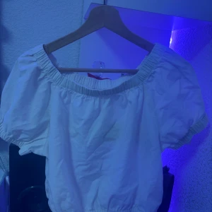 Vit offshoulder topp från Kappahl - Säljer en söt vit offshoulder topp från Kappahl med puffiga korta ärmar och resår vid halsringning och nederkant. Perfekt för en fräsch och somrig look. Tillverkad i mjuk bomull som känns skön mot huden.