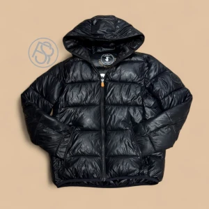 Save The Duck Jacka - Säljer nu denna svarta pufferjacka från Save The Duck med glansig finish och huva. Den är riktigt go och sitter najs. Den är 14Y i barn storlek och motsvarar XS. Perfekt nu inför vintern för ett kap!! Hör av er vid frågor eller flera bilder! Pytte litet hål längst ner på ryggen men inget som synns.