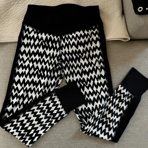 Svarta och vita zigzag leggings SOC - Snygga leggings från SOC i storlek 40 med svartvitt zigzag-mönster och svarta muddar vid bensluten. Hög midja och stretchigt material som passar perfekt för träning eller chill. Logga på benet och bekväm passform.