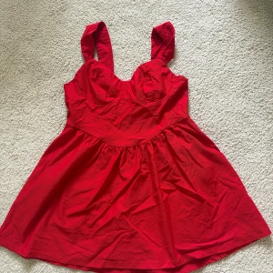 Röd kort klänning med breda axelband - Säljer en röd klänning med breda axelband och markerad byst. Kjolen är lätt utställd och klänningen har en feminin siluett. Storlek 2XL från SHEIN använd endast engång.