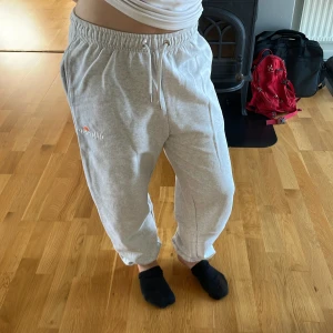 Grå mjukisbyxor från Ellesse - Säljer ett par ljusgrå mjukisbyxor från Ellesse med resår och snörning i midjan. Byxorna har en avslappnad passform och är tillverkade i mjukt bomullsmaterial. Liten broderad Ellesse-logga på ena benet. Perfekta för chill dagar eller när du vill vara bekväm.