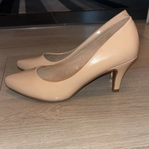 Beige klack från Alley - Snygga beige klack från Alley i storlek 37. Skorna har spetsig tå och är tillverkade i syntetmaterial med en slät finish. Perfekta för dig som gillar stilrena och klassiska klackar med modern touch.