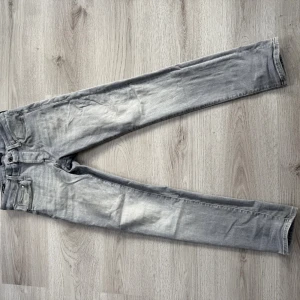 Grå slim jeans från Jack & Jones - Snygga grå jeans från Jack & Jones i modellen Slim/Glenn. Jeansen har en smal passform, klassisk femficksdesign och subtila slitningar för en cool look. Tillverkade i mjukt bomullsmaterial med stretch för extra komfort. Perfekta till sneakers och hoodie.