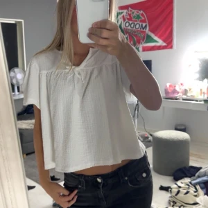 Vit croppad blus med knyt - Säljer en söt vit blus med korta ärmar och croppad passform. Toppen har en lätt textur i tyget och en liten knytning vid halsen som ger en gullig detalj. Perfekt att matcha med jeans eller kjol för en fräsch look.